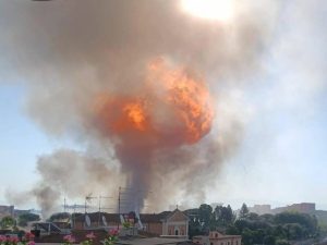 Explosión en Gasolinera: Vista de la gasolinera tras la explosión, con humo y daños visibles.