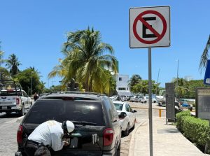Un agente de tránsito de Cancún emite una infracción a un vehículo estacionado sobre una banqueta.